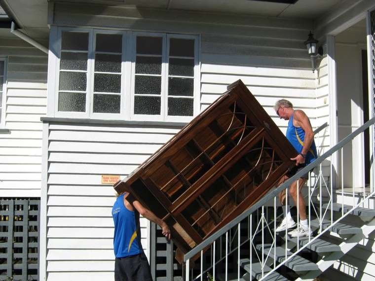 Two removalists carrying a large timber display cabinet down a set of front stairs