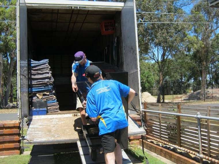 Two Wynnum Manly Removals crew members moving a heavy item on a trolley into the back of the truck