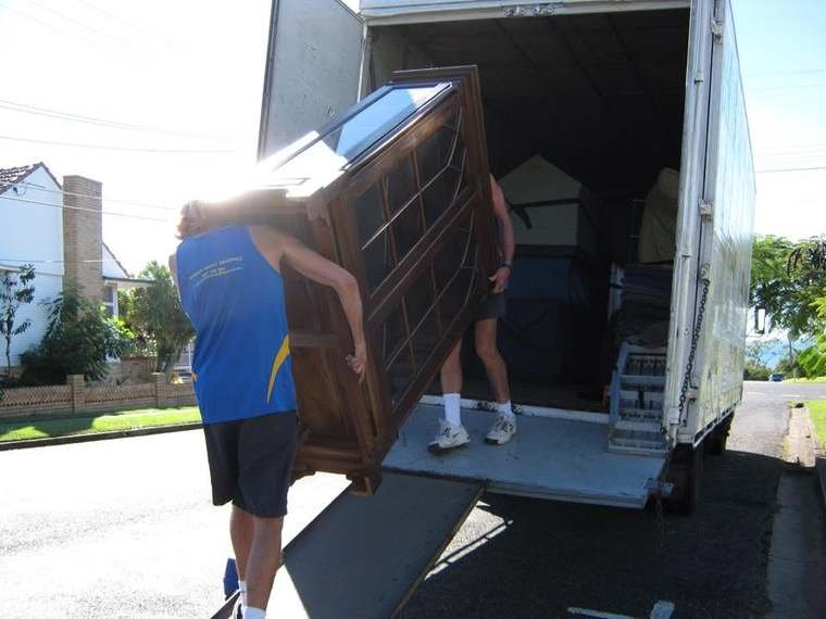 Removalists carrying a large timber cabinet up the ramp into the removals truck